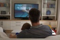 Rear view of father and son sitting at home together watching swimming competition on tv