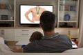 Rear view of father and sun at home together watching swimming competition on tv