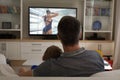 Rear view of father and sun sitting at home together watching swimming competition on tv