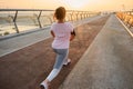 Rear view of a female athlete in sportswear stretching her legs muscles, performing lunges, working out on a city bridge in the