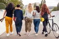 Rear View Of Female Friends With Skateboards And Bike Walking Through Urban Skate Park