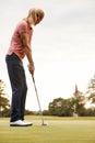 Rear View Of Female Golfer Putting Ball On Green