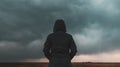 Rear view of female person wearing hooded jacket against dark moody dramatic clouds at sky