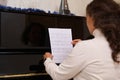 Rear view of a pianist holding notes of classic musical composition, sitting at black old piano, ready to play a melody