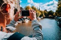 Rear view of female tourist taking photo of canal in Amsterdam on the mobile phone on sunny autumn day. Warm gold Royalty Free Stock Photo