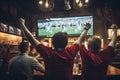 Rear view of football fans cheering with arms raised at bar counter, rear view Friends Watching Game In Sports Bar On Screens Royalty Free Stock Photo