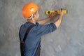 Rear view of a foreman in a helmet measuring the wall with a level. A construction worker checks the evenness of the