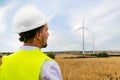 Rear view of foreman maintenance worker in wind turbine farm wearing helmet and safety vest. Copy space.