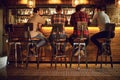 Rear view friends sitting on chairs talking at the bar in a bar. Royalty Free Stock Photo