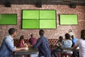 Rear View Of Friends Watching Game In Sports Bar On Screens