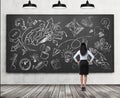 A rear view of a full length brunette lady who is looking at the black chalkboard with the sketched brainstorm process for busines