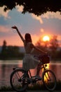 Rear view of girl with retro bike on which the basket enjoys the fiery sun at sunset Royalty Free Stock Photo