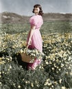 Rear view of a girl standing in a meadow holding a flower basket and smiling