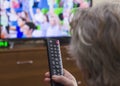 Rear view a gray-haired middle-aged woman controls the TV with a remote control Royalty Free Stock Photo