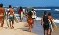 Rear view of a group of people walking carrying surfboards at the waters edge on Gilgo Beach