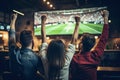 Rear view of a group of young people sitting in a pub and cheering while watching a football match, rear view Friends Watching Royalty Free Stock Photo