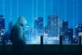 Rear view of hacker in black hoodie standing on the building terrace looking at cityscapes at night