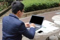 Rear view of handsome young business man is typing on the laptop against smartphone and documents on the top in public outdoors pa Royalty Free Stock Photo