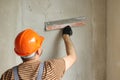 Rear view of handyman worker in overalls and protective helmet plastering concrete wall with putty using a big putty Royalty Free Stock Photo