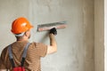 Rear view of handyman worker in overalls and protective helmet plastering concrete wall with putty using a big putty Royalty Free Stock Photo