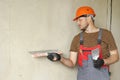 Rear view of handyman worker in overalls and protective helmet plastering concrete wall with putty using a big putty Royalty Free Stock Photo