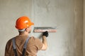 Rear view of handyman worker in overalls and protective helmet plastering concrete wall with putty using a big putty Royalty Free Stock Photo