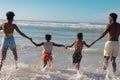 Rear view of happy african american parents holding children's hands running in sea against blue sky Royalty Free Stock Photo