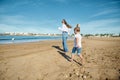 Rear view of a happy young mother and daughter smiling while running on the beach, leaving footsteps on the wet sand