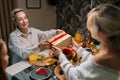 Rear view of happy young woman receiving gift from loving mother-in-law sitting with family at dinner feast table at Royalty Free Stock Photo