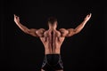 Rear view of healthy muscular young man with his arms stretched out isolated on black background Royalty Free Stock Photo