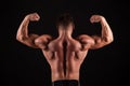 Rear view of healthy muscular young man with his arms stretched out isolated on black background Royalty Free Stock Photo