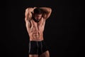 Rear view of healthy muscular young man with his arms stretched out isolated on black background Royalty Free Stock Photo