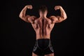 Rear view of healthy muscular young man with his arms stretched out isolated on black background Royalty Free Stock Photo