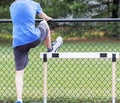 Hurdle runner performing a hurdle drill using a fence for support