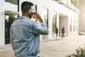 Rear view. Hipster businessman with beard, in denim jacket and trendy glasses walks around city and calls on phone. Royalty Free Stock Photo