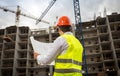 Rear view image of construction engineer looking at blueprints and working cranes on building site