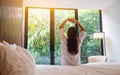 A woman do stretching after waking up in the morning , looking at a beautiful nature view outside bedroom