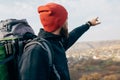 Rear view image of young hiker male wearing red hat, hiking in mountains, showing something to the horizon.