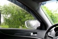 Rear view from inside mirror rain water drops falling on car window windshield glass with blurred trees nature background at