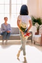 Rear view little daughter holding flowers and gift, congratulate mother