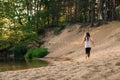 Rear view of little girl with long hair run on sandy beach near river in forest. Female child actively hike in nature. Royalty Free Stock Photo