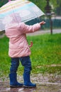 Rear view of a little girl in rubber boots with an umbrella in the pouring rain. Catches drops with the palm of your Royalty Free Stock Photo