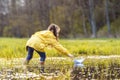 Rear view of girl standing in puddle and bending over closer to paper ship, trying to touch boat, swimming on water.