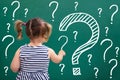 Little Girl Writing Question Marks On Chalkboard