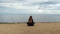 Rear view of long haired girl looking at seagulls. Concept. Back of young woman sitting on the sandy shore of lake, pond Royalty Free Stock Photo