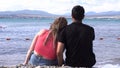 Rear view of loving couple sitting on stony shore in front of the sea. Media. Honeymoon concept, man and woman in love Royalty Free Stock Photo