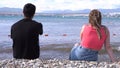 Rear view of loving couple sitting on stony shore in front of the sea. Media. Honeymoon concept, man and woman in love Royalty Free Stock Photo