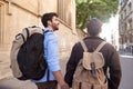 Rear View Of Male Gay Couple On Vacation Wearing Backpacks Holding Hands Walking Along City Street Royalty Free Stock Photo