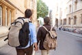 Rear View Of Male Gay Couple On Vacation Wearing Backpacks Holding Hands Walking Along City Street Royalty Free Stock Photo