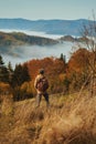 Rear view male hiker with backpack stands on mountain meadow, looking around, enjoys beautiful view Royalty Free Stock Photo